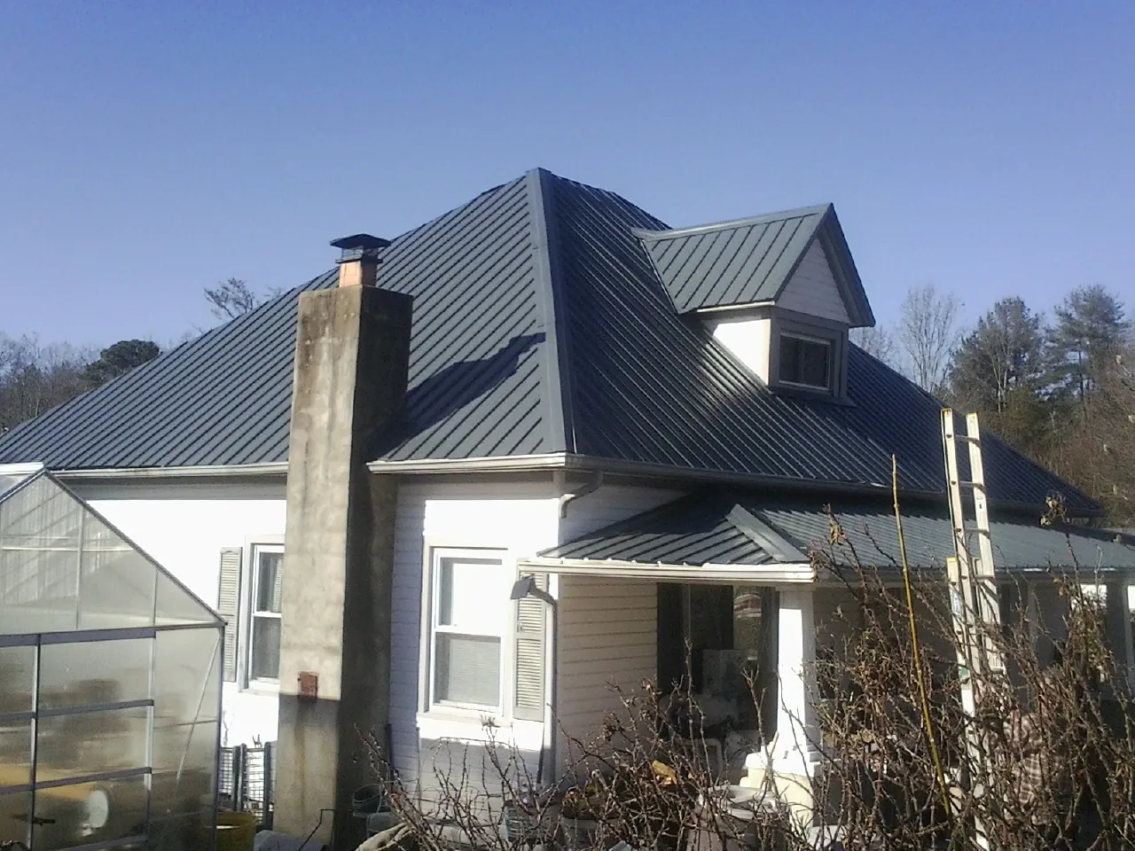 Dark blue standing seam metal roof on a white farmhouse with dormer — Slate & Tile Roof Repair by Roofing Brothers in Brackenridge