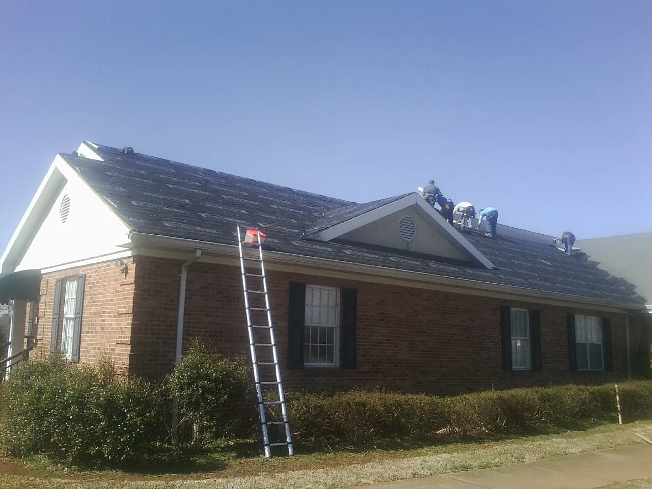 Crew tearing shingles off a brick ranch roof with a ladder set — Metal Roof Repair work by our crew in Brackenridge