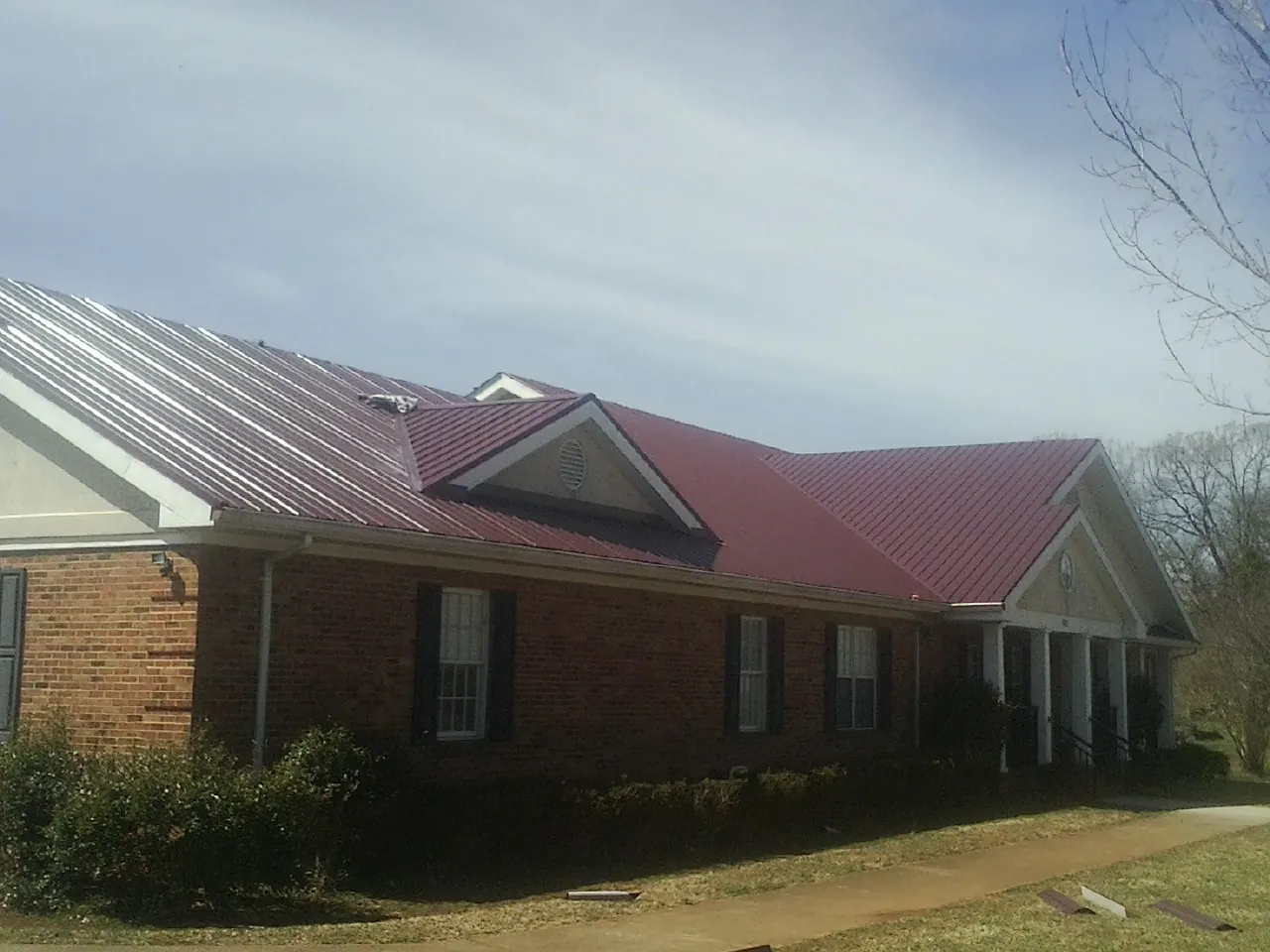 Red metal roof with gabled entries on a long brick building, from a Hail Damage Roof Repair job in Brackenridge