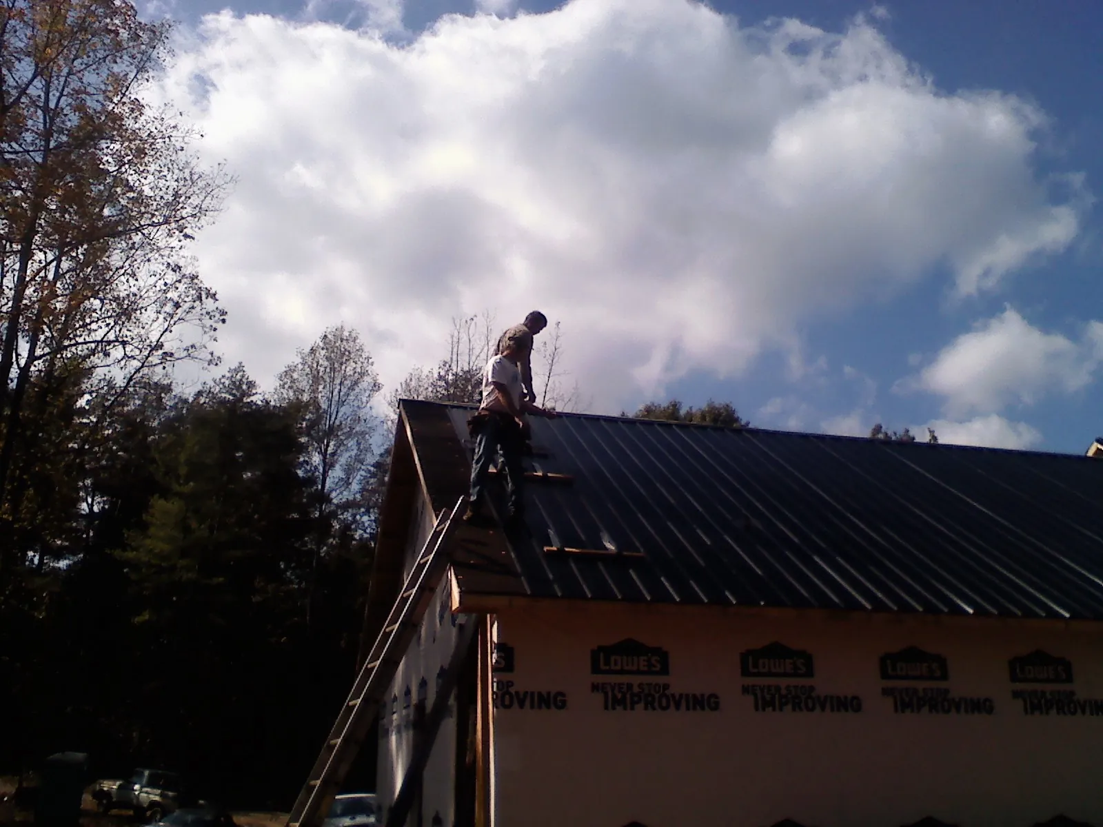 Roofer fastening dark metal panels high against a cloudy sky, from a Roof Inspection job in Brackenridge
