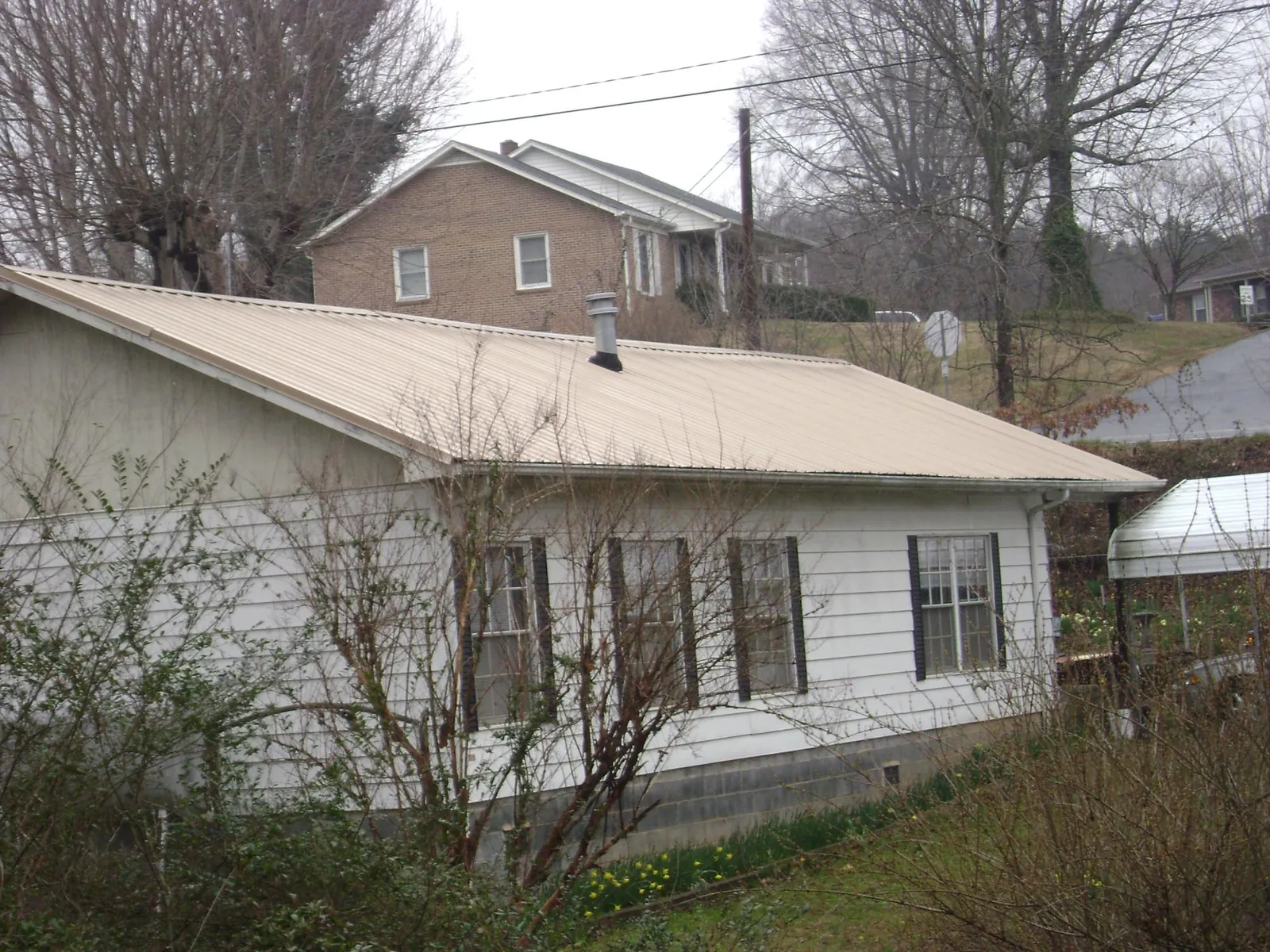 Tan metal roof on a white sided house set into a hillside — Commercial Roofing by Roofing Brothers in Brackenridge
