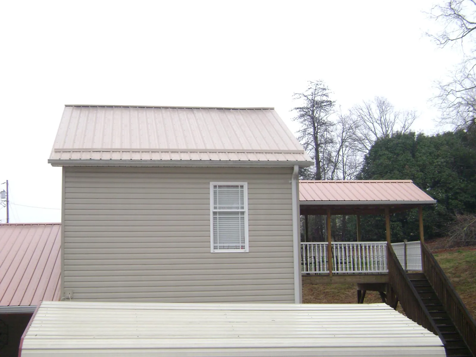 Tan metal roofs on a two story addition and attached porch, from a Roof Replacement job in Brackenridge